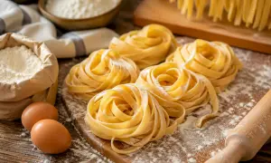 Nidi di pasta fatta in casa, farina, uova e mattarello su un tagliere di legno.