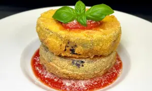 Due cordon bleu di melanzane impilati, dorati e croccanti, su salsa di pomodoro e basilico fresco.