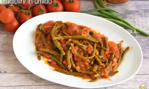 Fagiolini in umido, un piatto saporito con fagiolini verdi cotti in un sugo di pomodoro e cipolla, accompagnato da pomodorini freschi.
