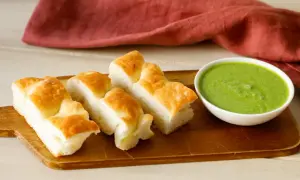 Focaccia tagliata a pezzi su tagliere di legno, accanto a una ciotola di pesto di salvia.