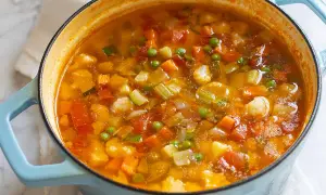 Un fumante minestrone di verdure in una pentola azzurra, ricco di carote, zucchine, piselli e cavolfiore.