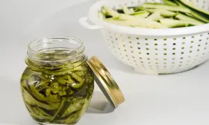 Barattolo di zucchine sott'olio, un modo gustoso per conservare le zucchine. In background, zucchine tagliate a julienne in uno scolapasta.