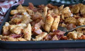 Straccetti di pollo al forno croccanti e saporiti, con fette di pancetta croccante, serviti in una teglia.