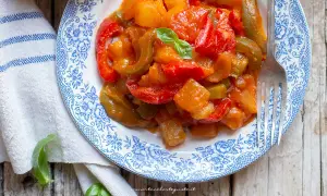 Un piatto di peperonata con patate, colorato e invitante, guarnito con basilico fresco.