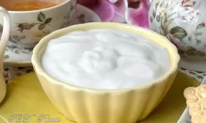 Una ciotola gialla piena di soffice crema al latte, accanto a una tazza di tè e fiori.