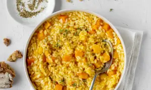 Un cremoso risotto con la zucca, guarnito con timo fresco e pepe nero macinato. Accanto, pane rustico e una ciotolina di pepe.