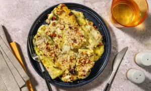 Parmigiana di zucchine gratinata con nocciole croccanti, servita su un piatto blu, con posate e un bicchiere di vino.