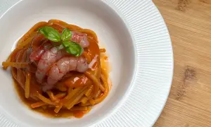 Spaghetti al sugo di pomodoro con gamberi freschi e basilico, un piatto che evoca il sapore intenso della bisque di gamberi.
