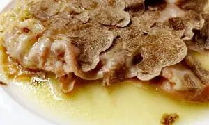 Cotoletta alla bolognese ricoperta di scaglie di tartufo, servita in un piatto bianco con una salsa dorata.