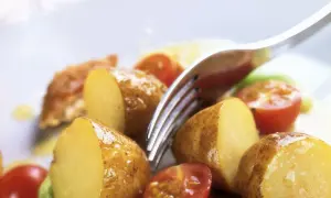 Patate novelle tagliate a metà, pomodorini e un tocco di verde compongono questa fresca insalata di patate estiva, pronta per essere gustata.