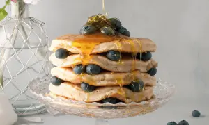 Pancake senza latte, una torre dorata con mirtilli freschi e sciroppo d'acero che cola. Delizioso e leggero, perfetto per ogni momento.