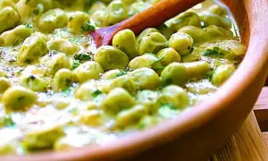 Un primo piatto saporito: piselli in umido, cremosi e profumati, serviti in una ciotola di legno con un cucchiaio.