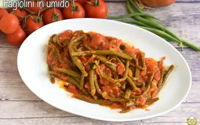 Fagiolini in umido, un piatto saporito con fagiolini verdi cotti in un sugo di pomodoro e cipolla, accompagnato da pomodorini freschi.