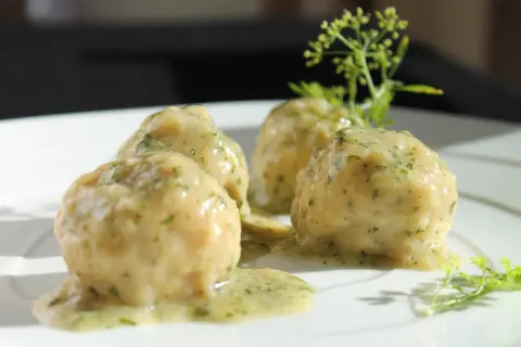 Quattro polpette in bianco su un piatto bianco, condite con una salsa cremosa e erbe aromatiche.