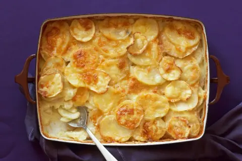 Parmigiana di patate dorata e cremosa, appena sfornata, con una fetta servita.