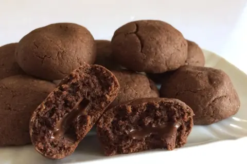 Biscotti al cioccolato morbidi con cuore filante. Alcuni sono interi, altri spezzati per mostrare il ripieno goloso.