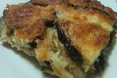 Una fetta di parmigiana di melanzane bianca, dorata e filante, con strati di melanzane e formaggio fuso.