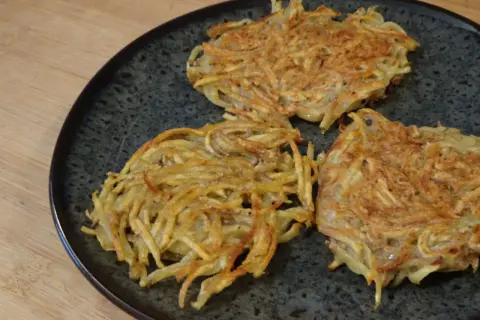 Tre croccanti rosti di patate in padella, dorati e pronti per essere gustati.