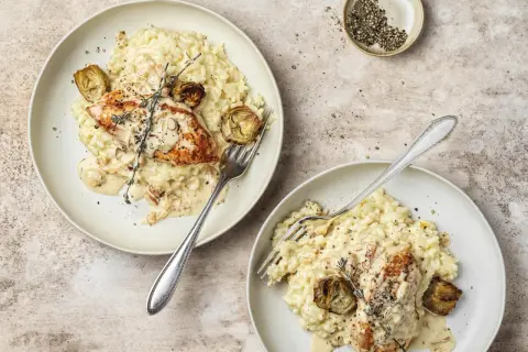 Due piatti di cremoso riso con pollo, guarniti con carciofi e rosmarino. Un piatto invitante e saporito.