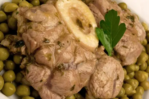 Ossobuco con piselli, un piatto succulento con carne tenera e piselli verdi brillanti, guarnito con una foglia di prezzemolo.