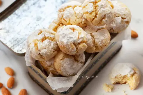 Biscotti con farina di mandorle, spolverati di zucchero a velo, in una scatola vintage. Alcune mandorle intere sono sparse intorno.