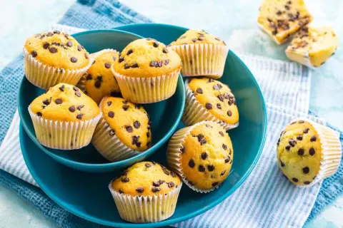 Muffin con gocce di cioccolato dorati e soffici, serviti in una ciotola blu.