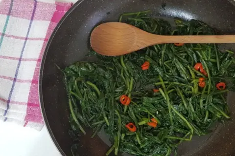Cicoria in padella, un contorno saporito con peperoncino e un cucchiaio di legno pronto a mescolare.