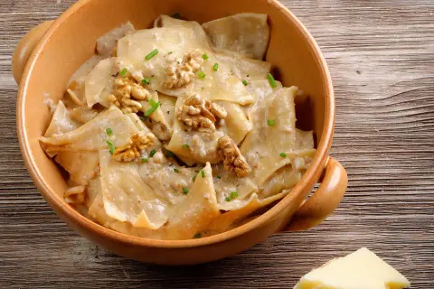 Pasta con cremoso pesto di noci, guarnita con noci intere e erba cipollina, servita in una ciotola di terracotta.