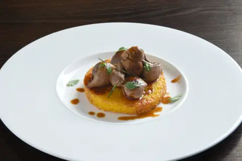Delizioso riso al salto con bocconcini di carne e salsa bruna, guarnito con erbe fresche su un piatto bianco.