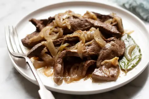 Piatto di fegato alla veneziana con cipolle caramellate, servito su un piatto bianco con una forchetta.
