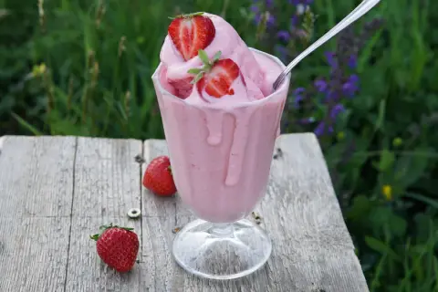 Un bicchiere di cremoso gelato alla fragola, guarnito con fragole fresche, su un tavolo di legno rustico.