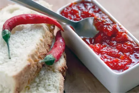 Fette di pane con peperoncini rossi e una ciotolina di marmellata di peperoncino, pronta per essere gustata.