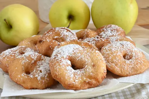 Frittelle di mele dorate e zuccherate, pronte per essere gustate. Tre mele verdi sullo sfondo.