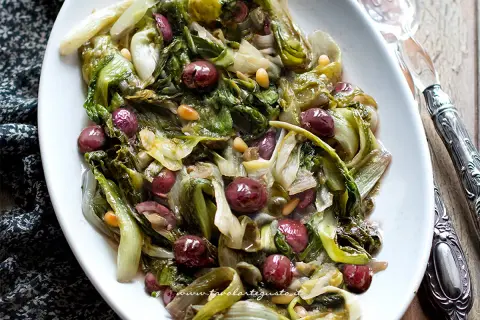 Scarola in padella con olive nere e pinoli, un contorno saporito e colorato, pronto per essere gustato.