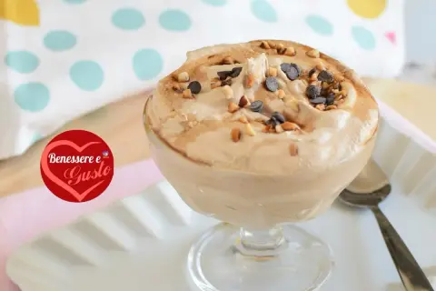 Deliziosa mousse al caffè, guarnita con nocciole tostate e gocce di cioccolato, servita in una coppa di vetro.