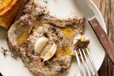 Succulenta braciola di maiale condita con aglio e erbe aromatiche, servita con pane croccante.