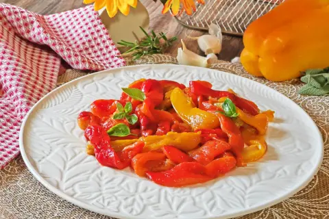 Peperoni rossi e gialli arrostiti in friggitrice ad aria, guarniti con basilico fresco, su un piatto bianco decorato.