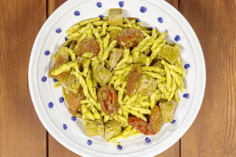 Piatto di trofie alla carlofortina con tonno, pomodorini secchi e pesto, servito su un piatto bianco con decorazioni blu.