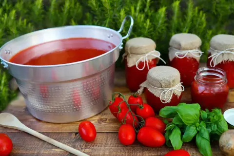 Un grande pentolone di passata di pomodoro, vasetti fatti in casa e pomodori freschi, pronti per la conservazione.