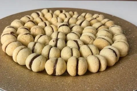 Baci di dama ricetta: biscotti friabili con ripieno di cioccolato, disposti a cerchio su un piatto dorato.