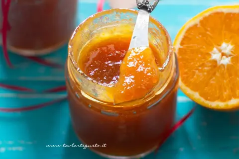 Un vasetto di marmellata di arance fatto in casa, con una fetta d'arancia accanto. La marmellata è lucida e invitante, pronta per essere gustata.