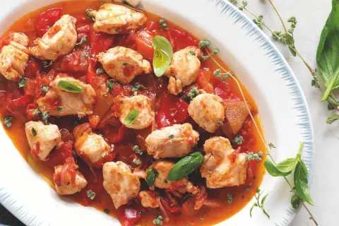 Piatto di coniglio alla cacciatora con pezzi di carne tenera in salsa di pomodoro e peperoni, guarnito con basilico fresco e erbe aromatiche.