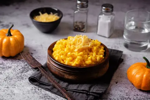 Un invitante piatto di pasta e zucca, guarnito con formaggio grattugiato, accanto a piccole zucche arancioni.