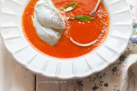 Una cremosa zuppa di pomodoro, arricchita da due quenelle di burrata e foglie di basilico fresco. Un piatto invitante e gustoso.