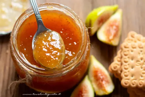 Un cucchiaio raccoglie la deliziosa marmellata di fichi da un barattolo, accanto a fichi freschi e biscotti.