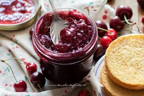 Un barattolo pieno di marmellata di ciliegie fatta in casa, con ciliegie fresche e fette biscottate.