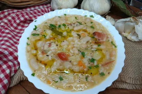 Un piatto fumante di riso e fagioli, condito con olio d'oliva e prezzemolo, con aglio e una tovaglia a scacchi sullo sfondo.