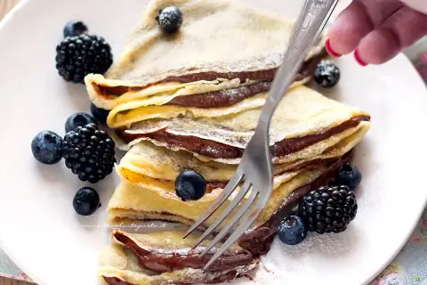Piatto di crepes alla Nutella, guarnite con mirtilli e more, pronte per essere gustate.