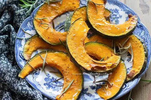Fette di zucca in friggitrice ad aria, dorate e profumate al rosmarino, servite su un piatto blu e bianco.