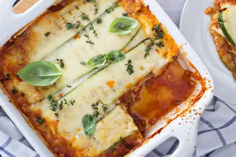 Lasagne di zucchine al forno, dorate e filanti, guarnite con basilico fresco e timo. Un piatto leggero e gustoso.